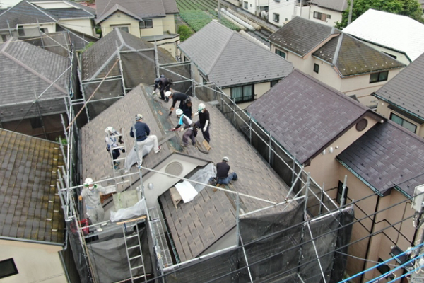 足場の組まれた戸建ての屋根で職人たちが作業を行う様子