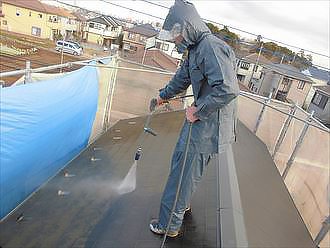 屋根の上で防護服を着て高圧洗浄を行います
