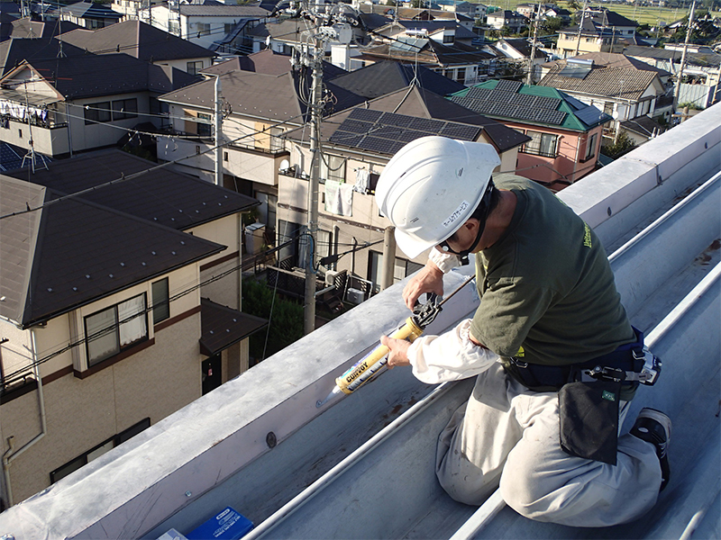 折板屋根でコーキング補修する職人